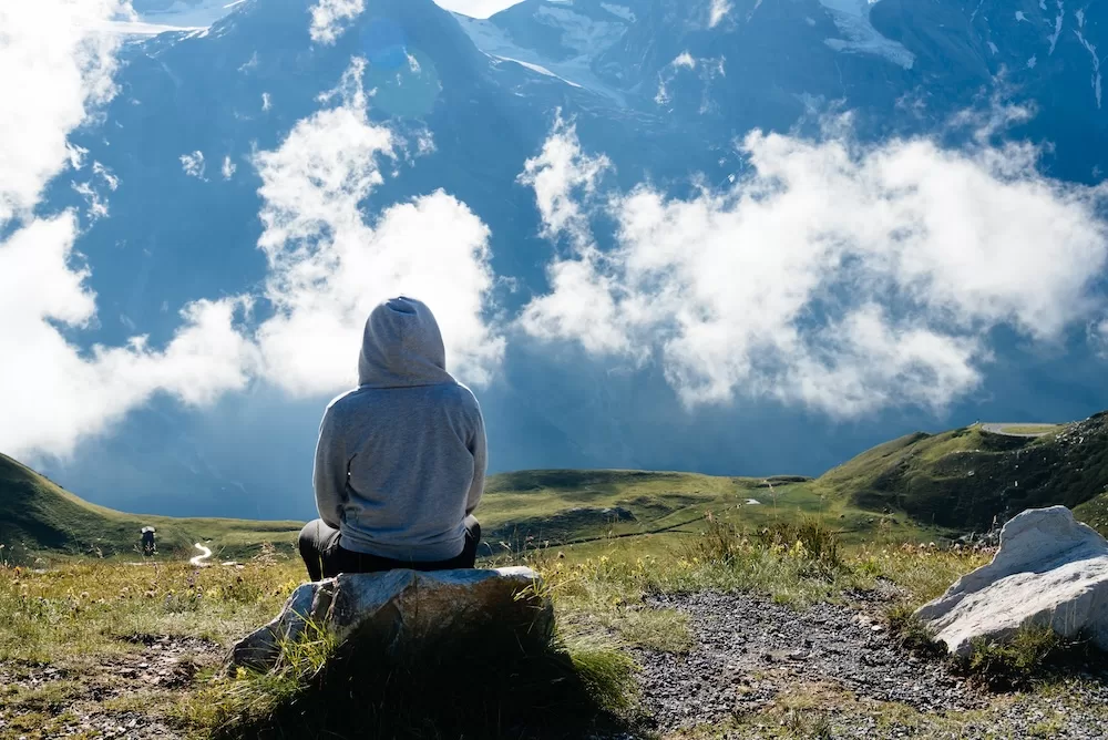 Young woman sitting looking at sea of clouds in mountain landscape Young woman sitting looking at sea of clouds in mountain landscape. Rear view. Grossglockner, Austria.